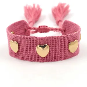 Detail of pink woven bracelet with golden metal hearts and adjustable tassel closure
