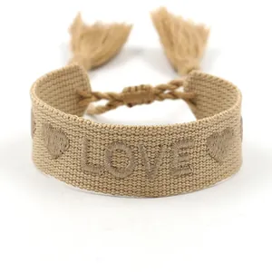Detail of woven khaki bracelet featuring LOVE embroidery and adjustable tassels