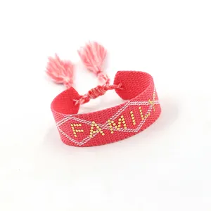 Close-up of pink woven adjustable bracelet with gold FAMILY text and red tassels