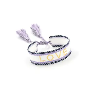 Detail of woven white friendship bracelet with purple trim, yellow LOVE text and tassels