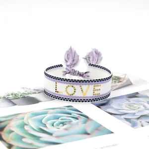 Macro detail of hand-woven bracelet with LOVE embroidery and purple tassel drawstrings