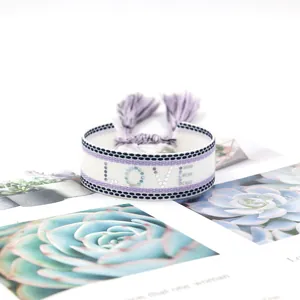 Detail of woven love bracelet showing purple embroidery and adjustable fringe tassels