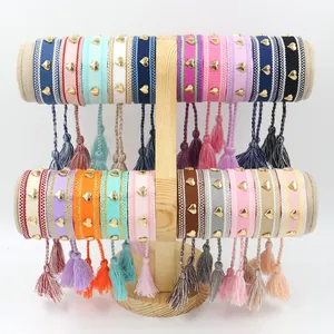 Handmade woven bracelet with golden heart rivets and tassels on wooden display stand