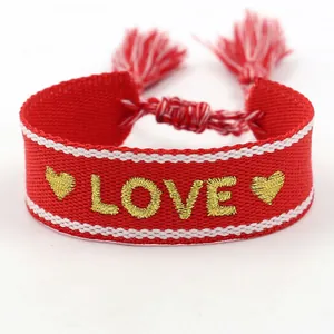 Detalle de pulsera de la amistad roja tejida a mano con bordado LOVE dorado y borlas