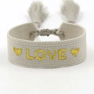Detalle de una pulsera tejida bohemia con bordado LOVE dorado y adornos de borlas