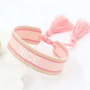 Detailed view of pink hand-woven embroidery bracelet featuring NICE text and fringe tassels