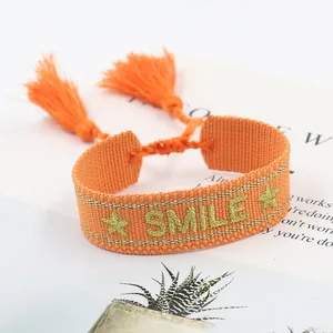 Detail of orange woven bracelet with gold SMILE embroidery and decorative tassels