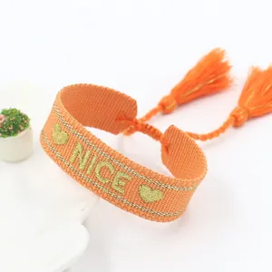 Detailed view of orange woven bracelet with gold embroidered NICE letters and tassels