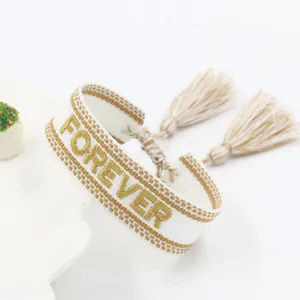 Handcrafted woven bracelet with Forever embroidery and tassels on white background