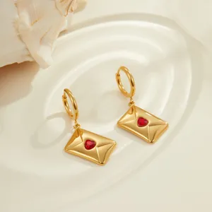 Boucles d'oreilles enveloppe dorées avec zircon cœur rouge sur fond texturé eau