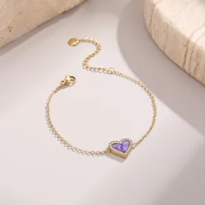 Détail d'un bracelet cœur doré avec incrustation violette et cristaux sur fond pierre