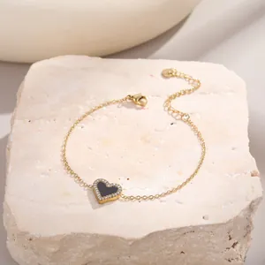 Détail d'un bracelet doré avec pendentif cœur noir serti de zircons étincelants