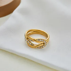 Detail van een vergulde gedraaide ring met witte zirkonia op wit getextureerde stof