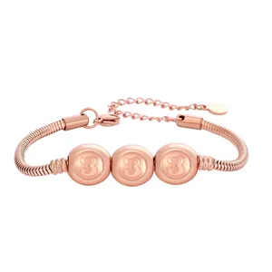Détail d'un bracelet serpent or rose avec perles gravées du chiffre trois et chaîne d'extension