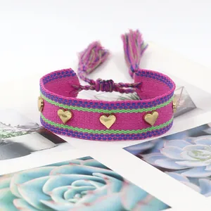Detail of hand-woven magenta friendship bracelet with golden heart studs and tassels