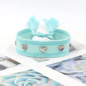 Détail du bracelet tissé bleu clair avec clous en cœur argentés et finitions à franges