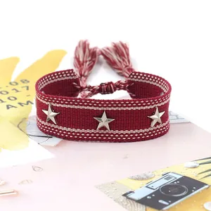 Detalle de pulsera tejida burdeos con tachuelas de estrella y lazos de flecos suaves