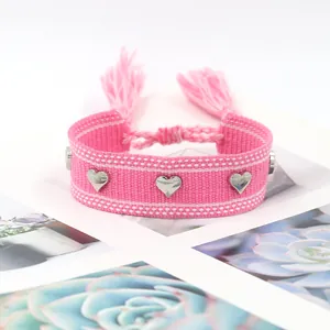 Détail du bracelet tissé rose avec clous en cœur argentés et breloques à pompons