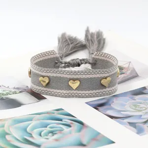 Close-up of woven heart bracelet with golden rivets and boho tassel detail