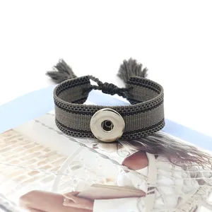 Detalle de pulsera de lona tejida verde oliva con botón a presión y borlas de flecos