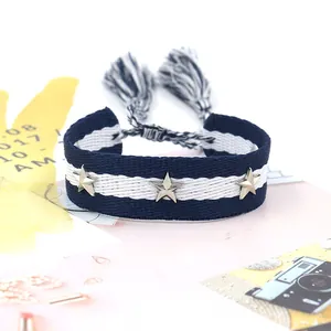 Detalle de pulsera tejida a rayas azules y blancas con estrellas de plata y borlas