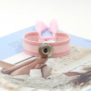 Détail d'un bracelet tressé rose avec bouton-pression argenté et pompons décoratifs