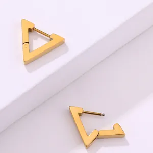 Detalle de pendientes de aro triangulares de oro pulido sobre soportes geométricos blancos