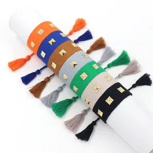 Détail de bracelets tissés colorés avec rivets pyramides dorés et finitions à pompons