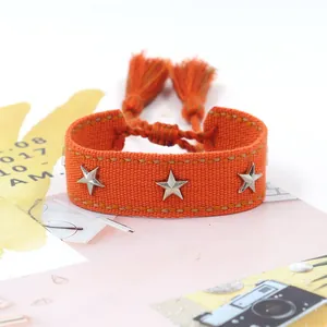 Detalle de pulsera tejida naranja con tachuelas de estrella plateadas y borlas ajustables
