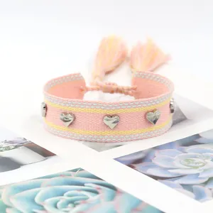Détail d'un bracelet tissé rose et jaune orné de clous coeur argentés et de glands
