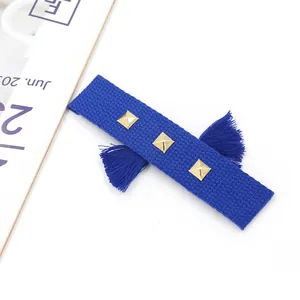 Détail d'un bracelet tissé bleu foncé avec trois clous dorés et des pompons latéraux