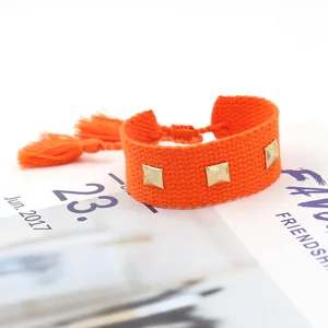 Détail d'un bracelet tissé orange avec des clous pyramides dorés et des pompons