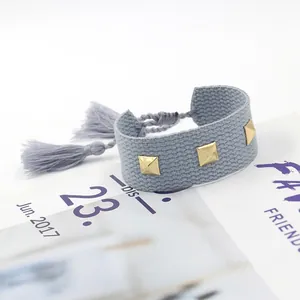 Détail d'un bracelet tissé bleu-gris avec trois clous dorés et des pompons élégants