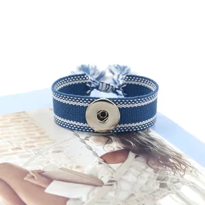 Detalle de pulsera Noosa tejida en azul y blanco con botón de presión y borlas largas