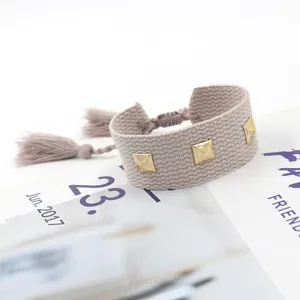 Détail d'un bracelet tissé ajustable avec des clous dorés et des pompons décoratifs
