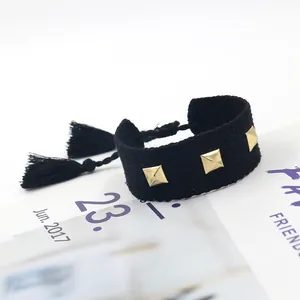Détail d'un bracelet en coton tissé noir avec des clous dorés carrés et des franges