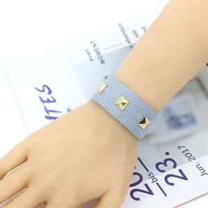 Détail du bracelet punk tissé bleu clair avec clous pyramides dorés sur le poignet