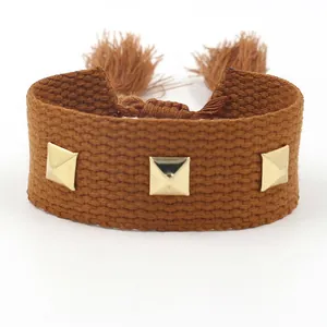 Bracelet tissé marron avec clous pyramidaux dorés et glands sur un fond blanc neutre