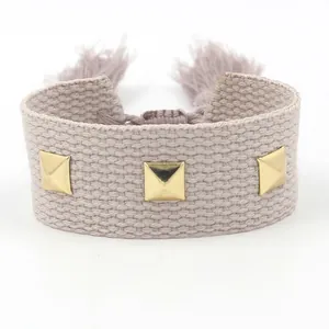 Bracelet tissé beige réglable avec clous pyramides dorés et glands sur fond blanc