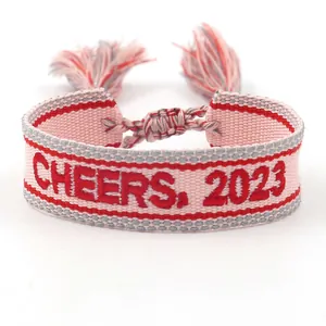 Pink and red embroidered woven bracelet featuring CHEERS 2023 text and tassels