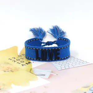 Detail of navy blue woven LOVE bracelet with yellow stitching and decorative tassels