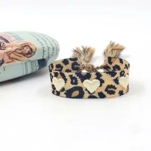 Gros plan d'un bracelet tissé léopard avec broderie cœur blanc et cordon à pompons