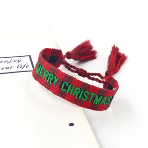 Detail of embroidered Merry Christmas woven bracelet with festive red tassels and adjustable cord