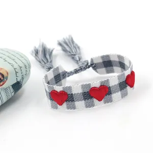 Gros plan de cœurs brodés rouges sur bracelet tissé à carreaux gris avec pompons