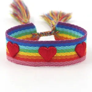 Gros plan de cœurs rouges brodés sur un bracelet d'amitié tissé arc-en-ciel avec franges