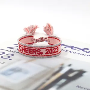 Detail of hand-woven friendship bracelet with red Cheers 2023 text and pink tassels