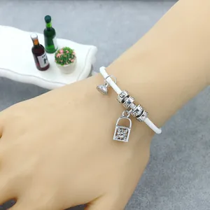 Détail du bracelet tressé blanc avec perle trèfle, pendentif cadenas et petite cloche