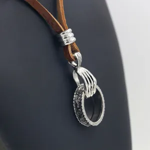 Close-up of vintage silver hand claw pendant holding an engraved ring on brown leather cord