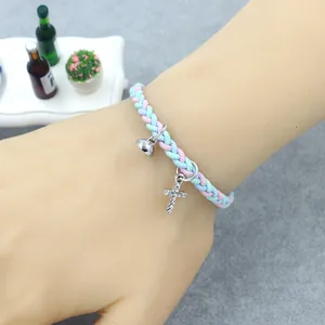 Détail du bracelet tressé avec pendentif croix et clochette porté sur le poignet