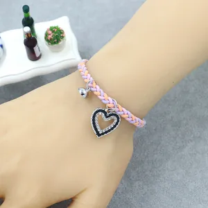 Detail of woven bracelet with orange-purple cords, silver bell, and rhinestone heart charm